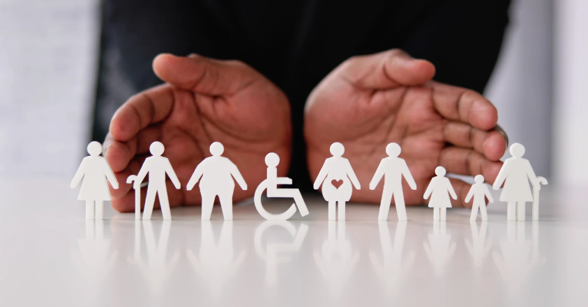 Different symbols of disability represented as paper cut outs with a hand cupping them all